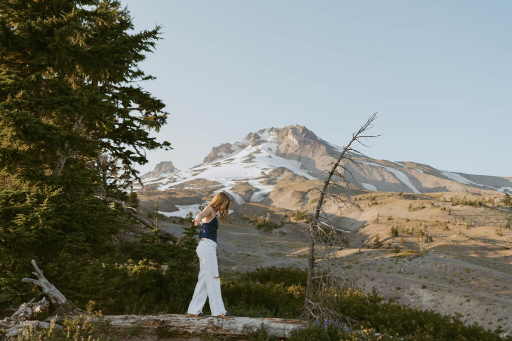 A senior is standing on a log in front of a mountain.