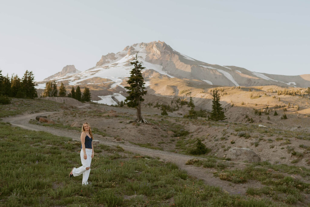 A woman is standing in a field with a mountain in the background.