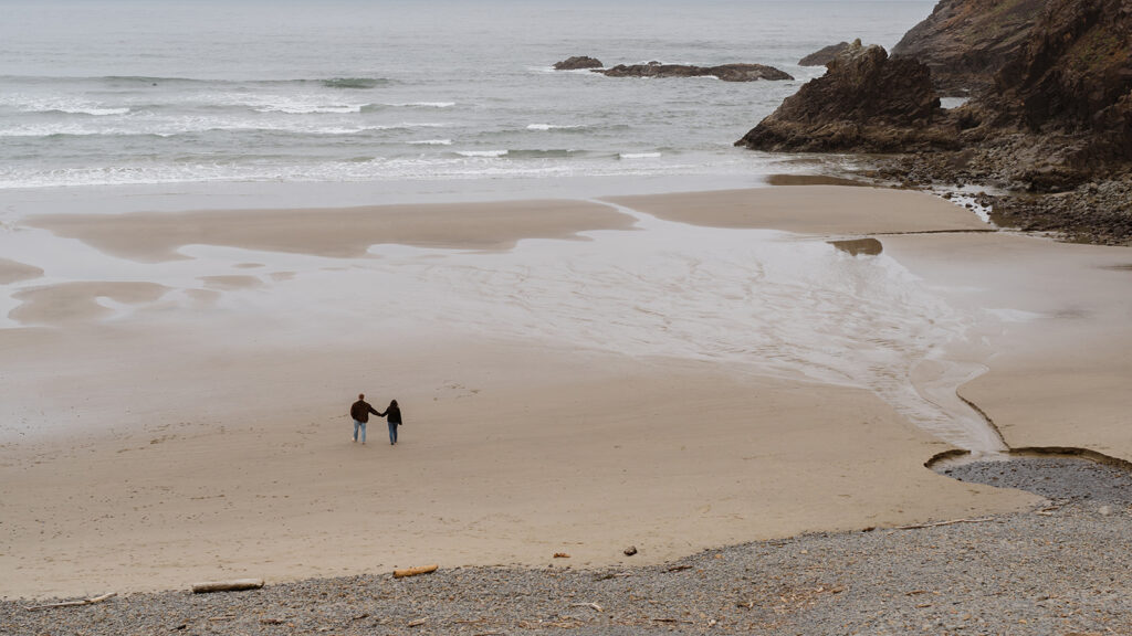 Couple walking hand in hand along a wide, empty beach