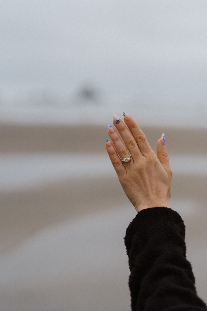 Hand raised showing engagement ring with beach in background