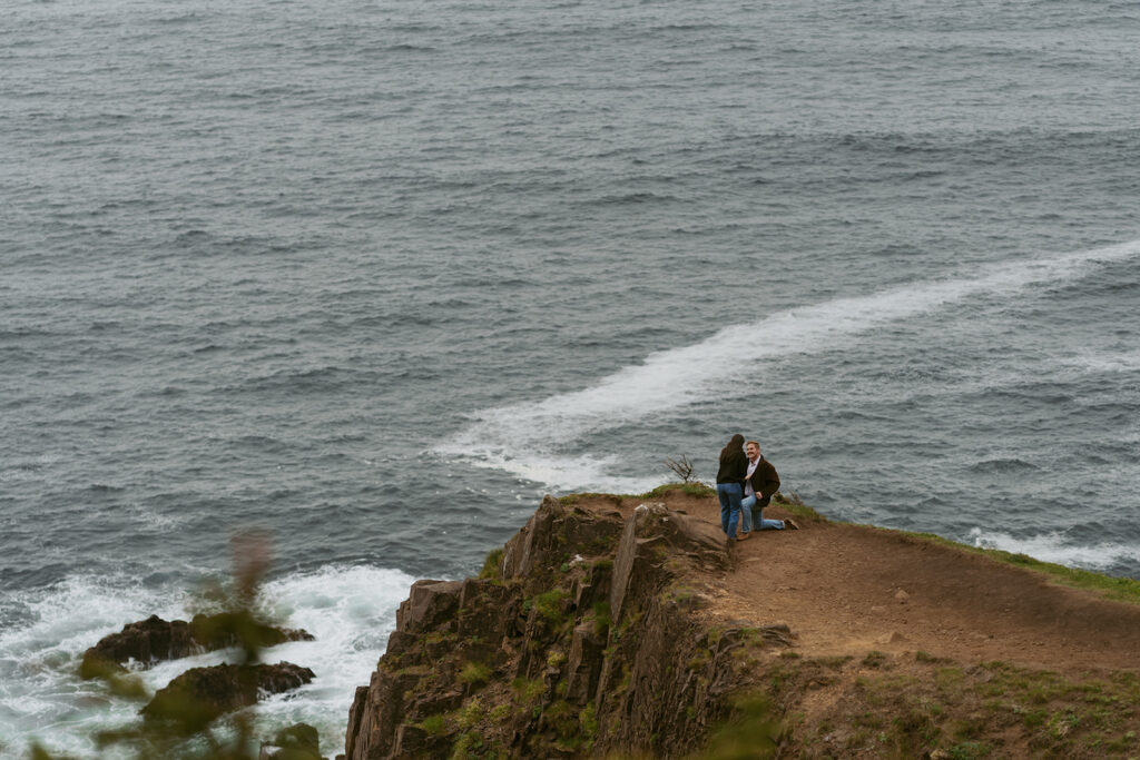 Couple standing together at the edge of a cliff overlooking the water