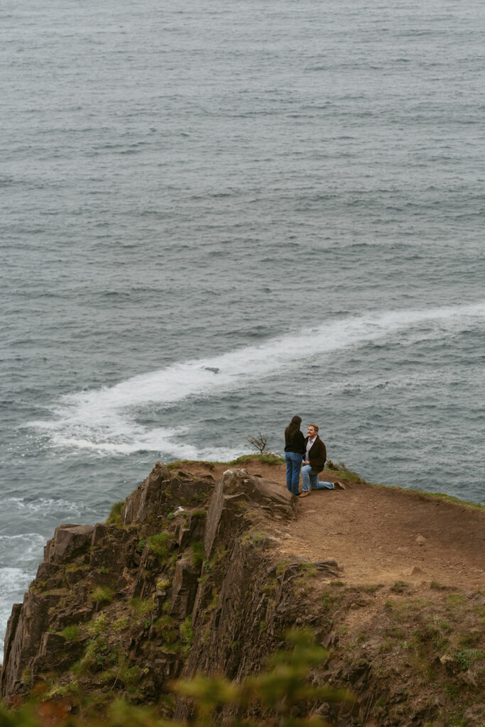 Person kneeling to propose on a cliff edge with ocean waves in the background