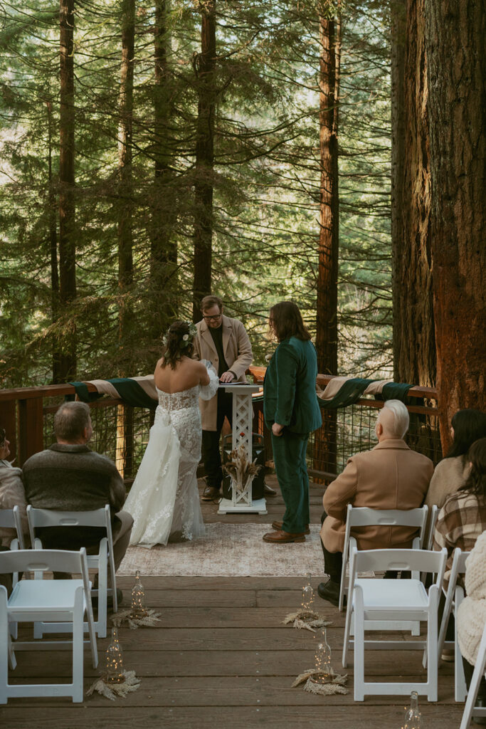 Bride and groom exchange vows on a forest deck surrounded by guests