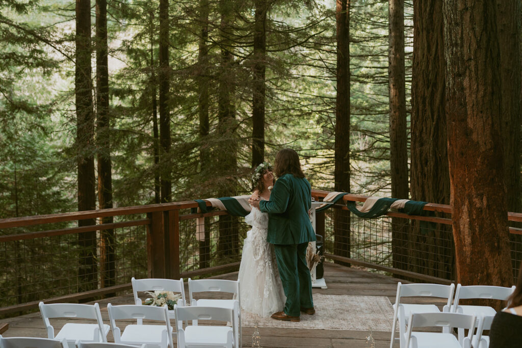 Bride and groom share a kiss on a forest deck surrounded by redwoods at Hoyt Arboretum
