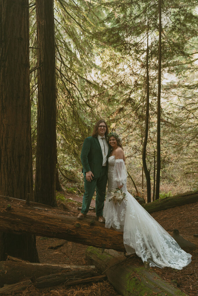 Bride and groom pose together on a mossy log in the woods