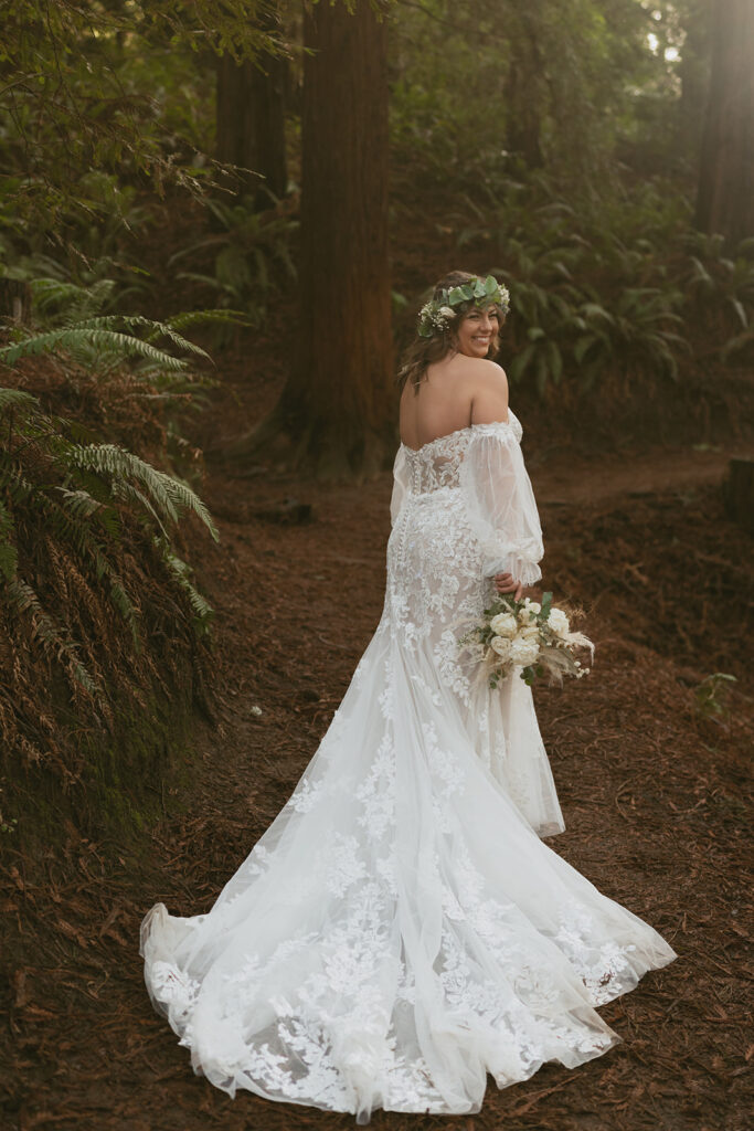 Bride looks back showing lace train of her gown in the woods