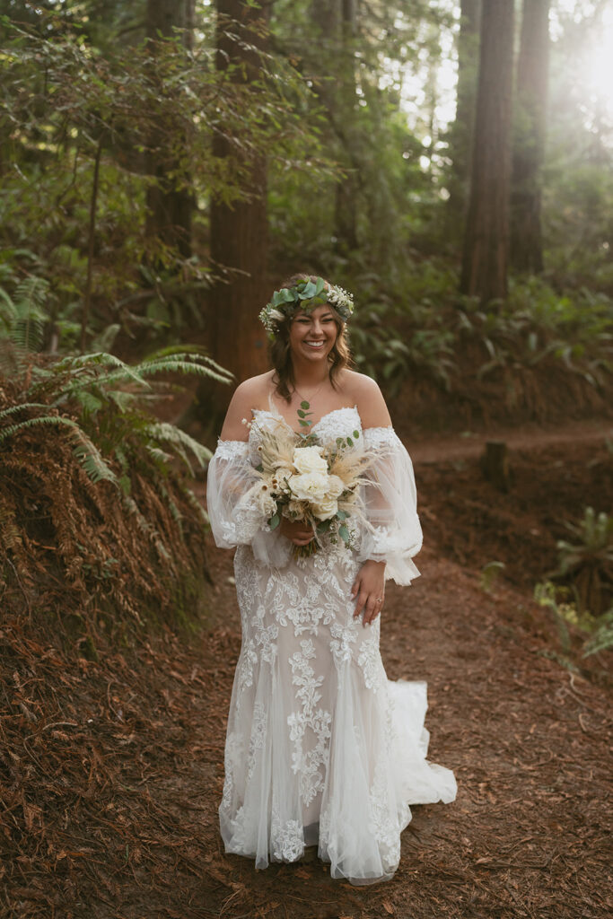 Bride smiles holding bouquet on a forest trail