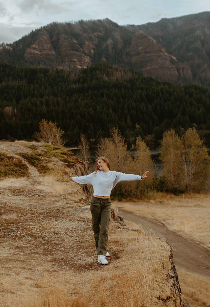 High school senior with outstretched arms on mountain trail in Portland
