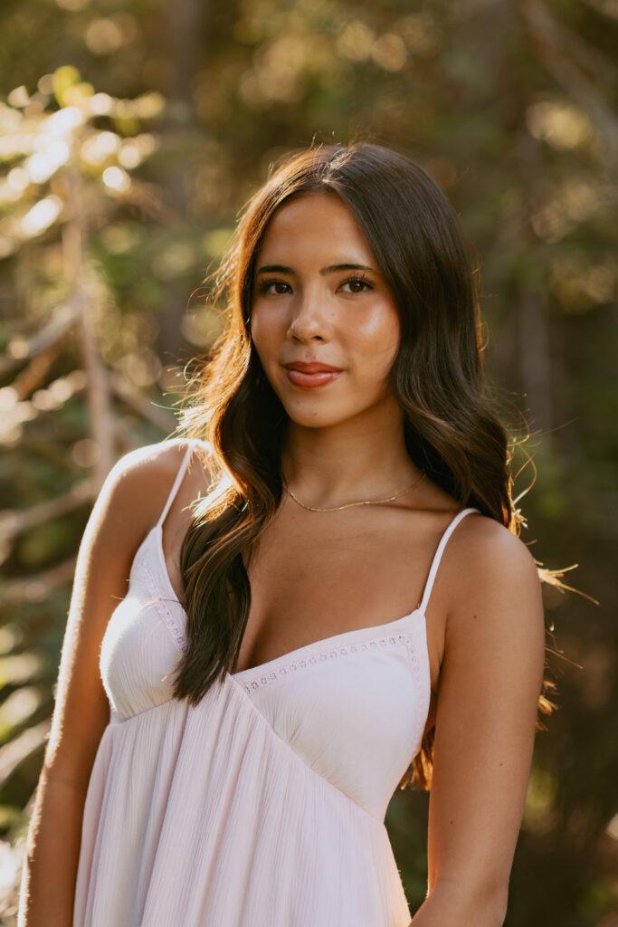 Natural light senior portrait of brunette girl in white spaghetti strap dress with warm golden hour lighting at Mount Hood location
