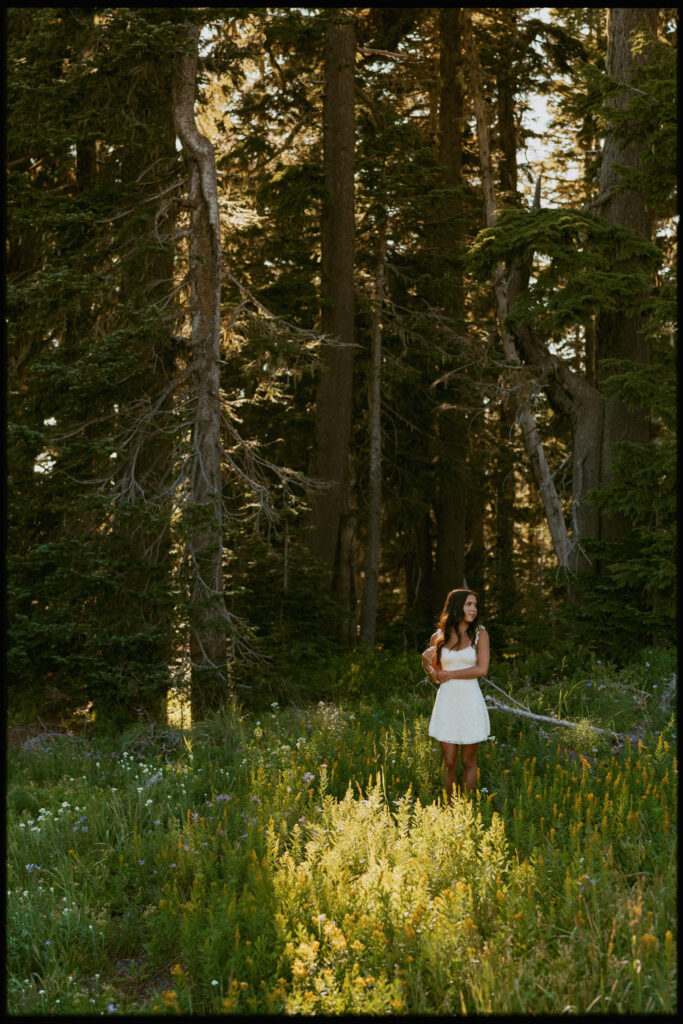 Mount Hood senior session in tall pine forest with girl in white strapless dress standing among towering evergreen trees and wildflowers