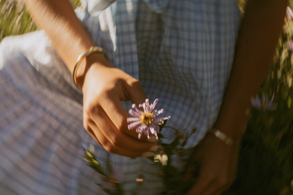 Close-up detail of senior girl's hand holding small purple wildflower with gold bracelet during Mount Hood outdoor portrait session