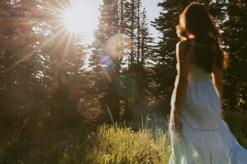 Senior girl in white flowing dress walking through Mount Hood wildflower meadow at golden hour