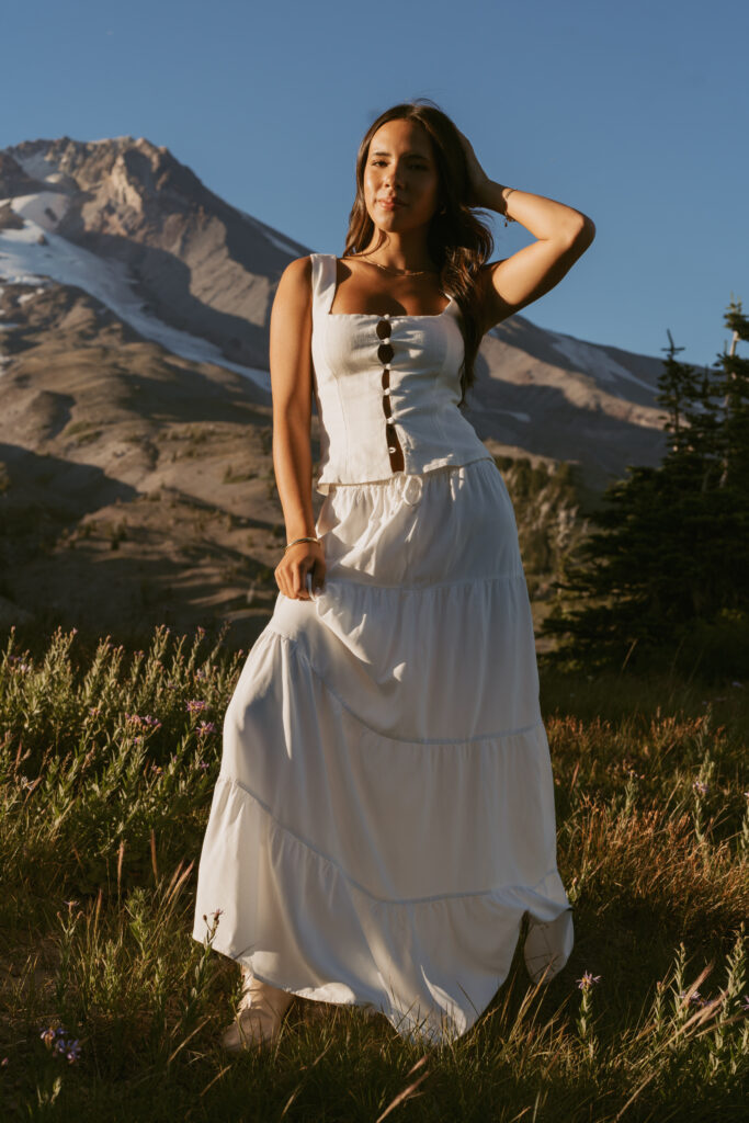 girl in white lace-up corset and flowing skirt with snow-capped mountain backdrop and alpine meadow