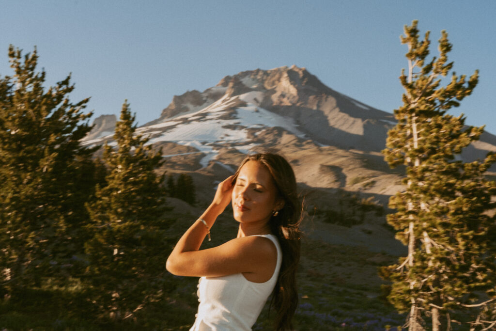 girl in white tank top with mountain peak backdrop during summer wildflower season booking information