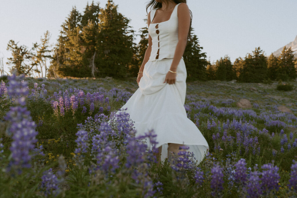 girl in white dress dancing through purple lupine wildflower field during peak bloom season