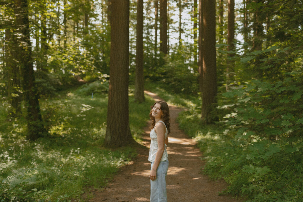 Natural light senior photos in Portland forest showing girl in white top and jeans on woodland trail at Hoyt Arboretum