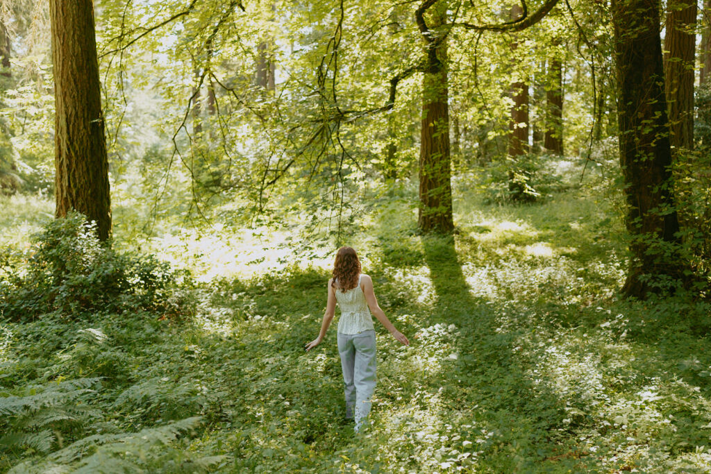 Hoyt Arboretum senior portrait with girl in white outfit walking through sun-dappled Pacific Northwest forest trail