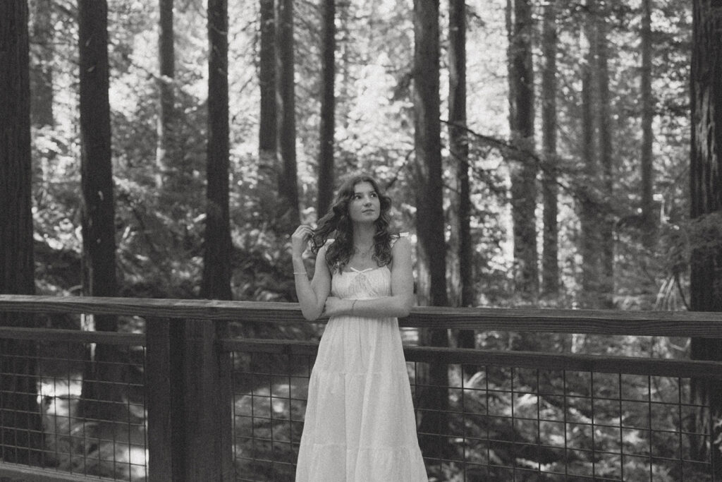 Hoyt Arboretum Portland senior black and white photo featuring girl in white dress twirling hair along wooden fence