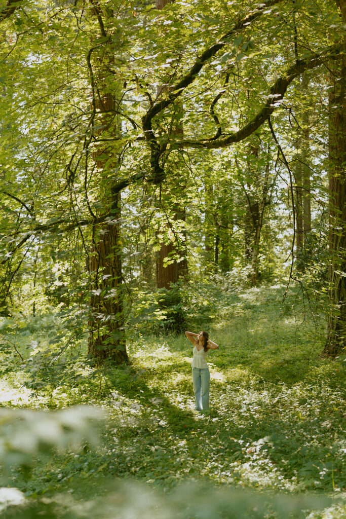 Hoyt Arboretum senior portrait with girl in white top and blue jeans walking through sun-dappled Pacific Northwest forest trail