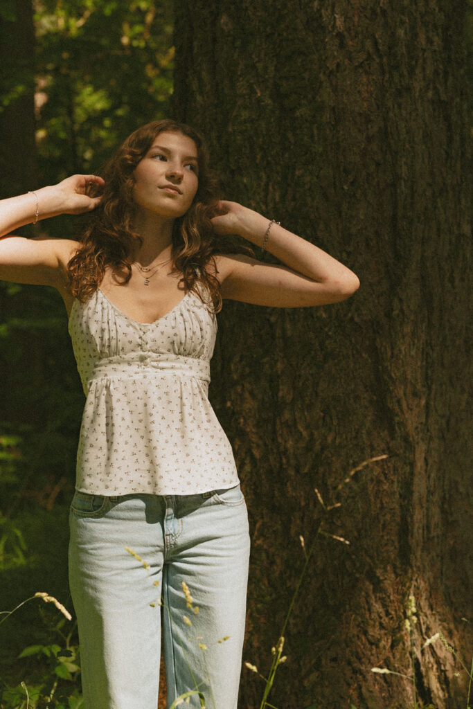 Hoyt Arboretum Portland senior photos featuring girl in white top and blue jeans standing next to shaded redwood trunk in sunlight 