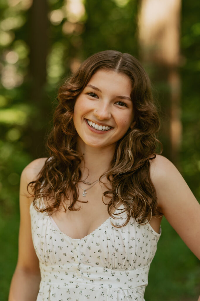 Natural light senior headshot of brunette girl in white polka dot top with curly hair at Hoyt Arboretum forest location