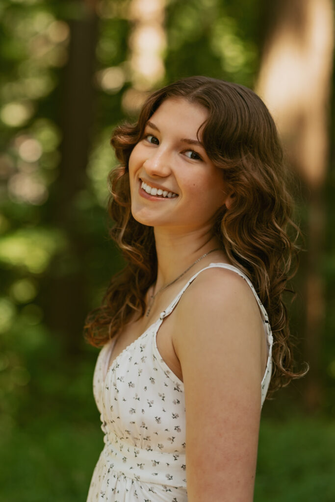 Golden hour senior portrait of girl in white polka dot dress with warm forest lighting at Hoyt Arboretum Portland