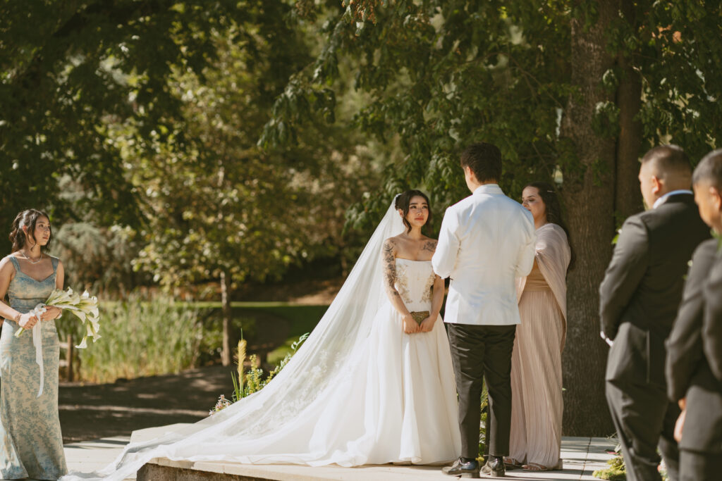 Bride and groom exchange vows under trees at aurora colony vineyards