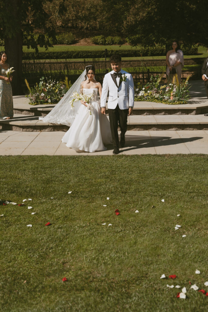 couple walks away from vineyard ceremony with rose petals