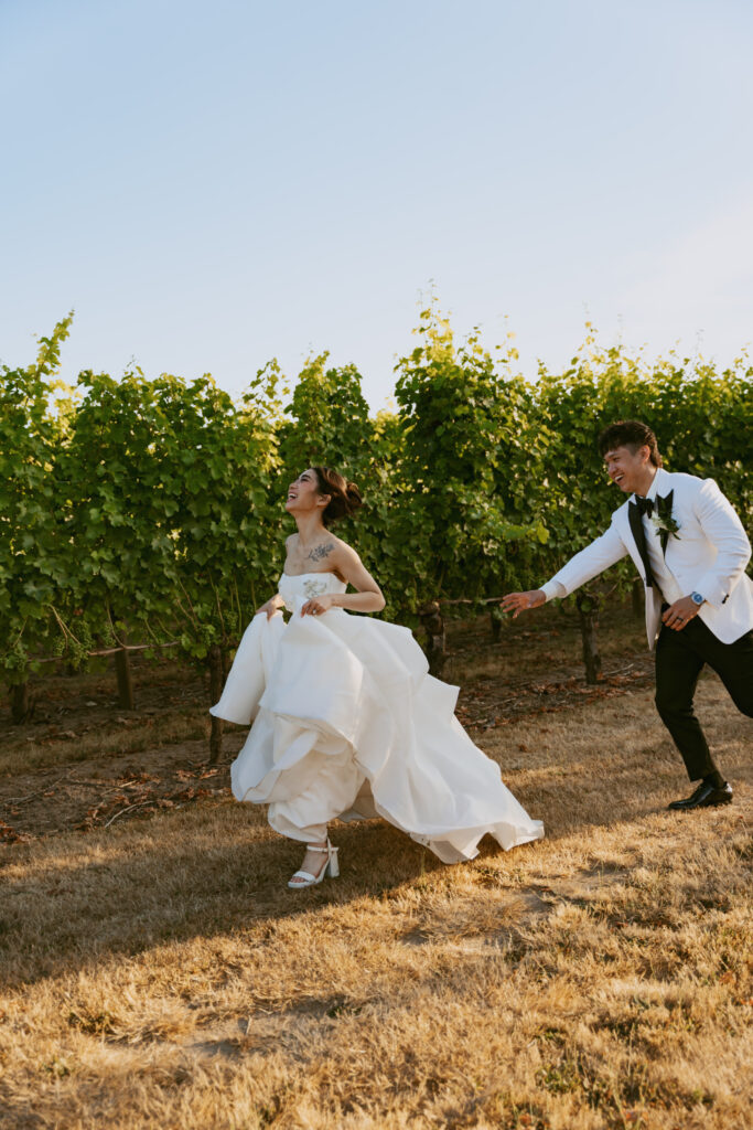 Groom helps bride run through vineyard rows during their micro wedding