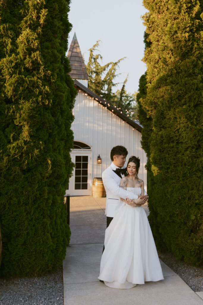 Bride and groom embrace between tall hedges