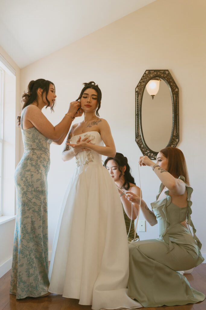Bridesmaids help bride get ready in white room at Aurora Colony Vineyards
