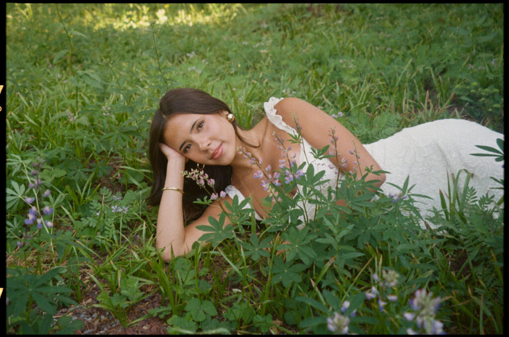 Woman in white dress lies in wildflower meadow in Oregon