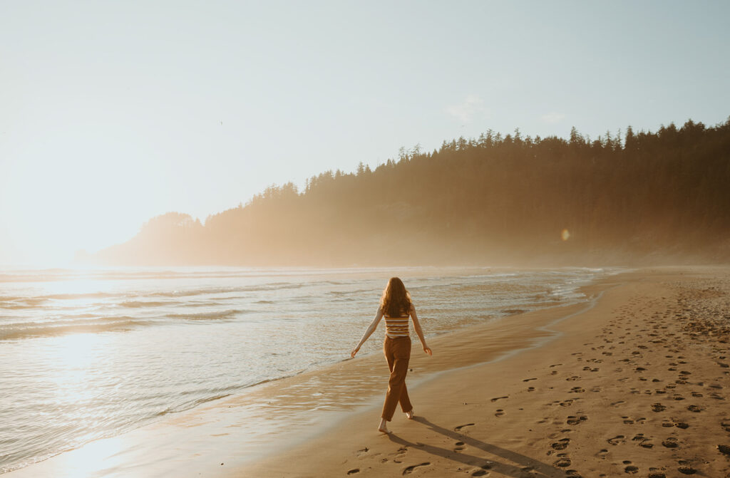 Silhouetted woman walks beach at sunset in Oregon
