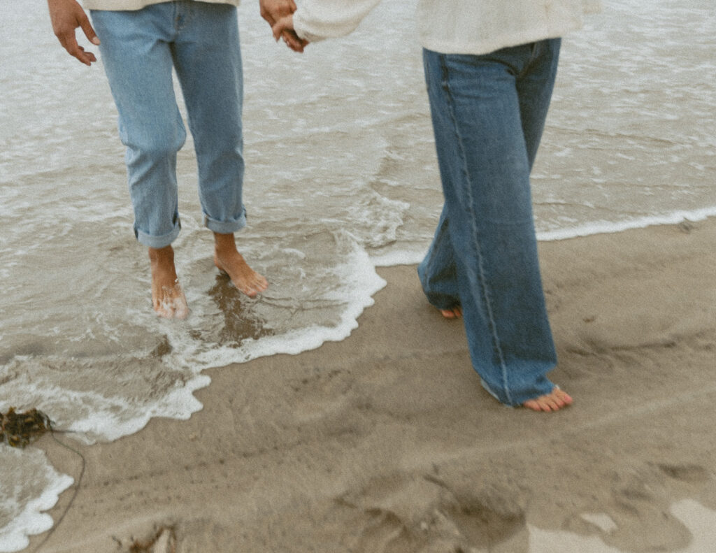 Couple holding hands and walking barefoot at the edge of the ocean