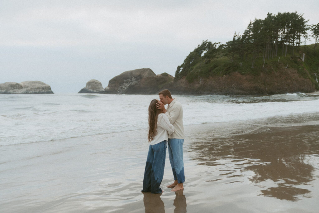 Jentrie and Brayden kissing on the shoreline with waves behind them