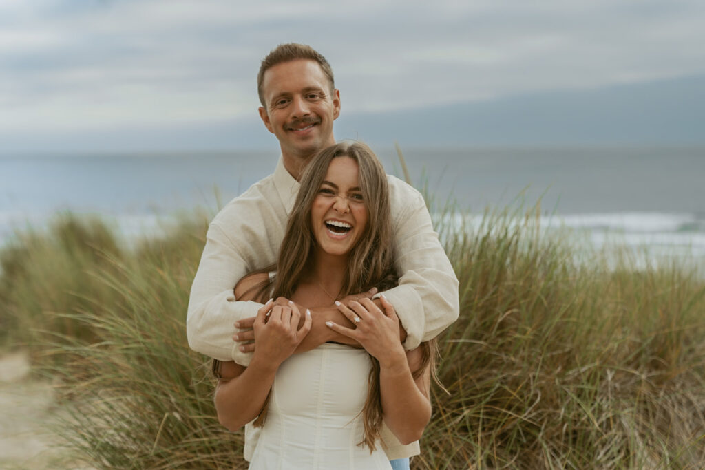 Jentrie and Brayden hugging from behind as they laugh on the dunes