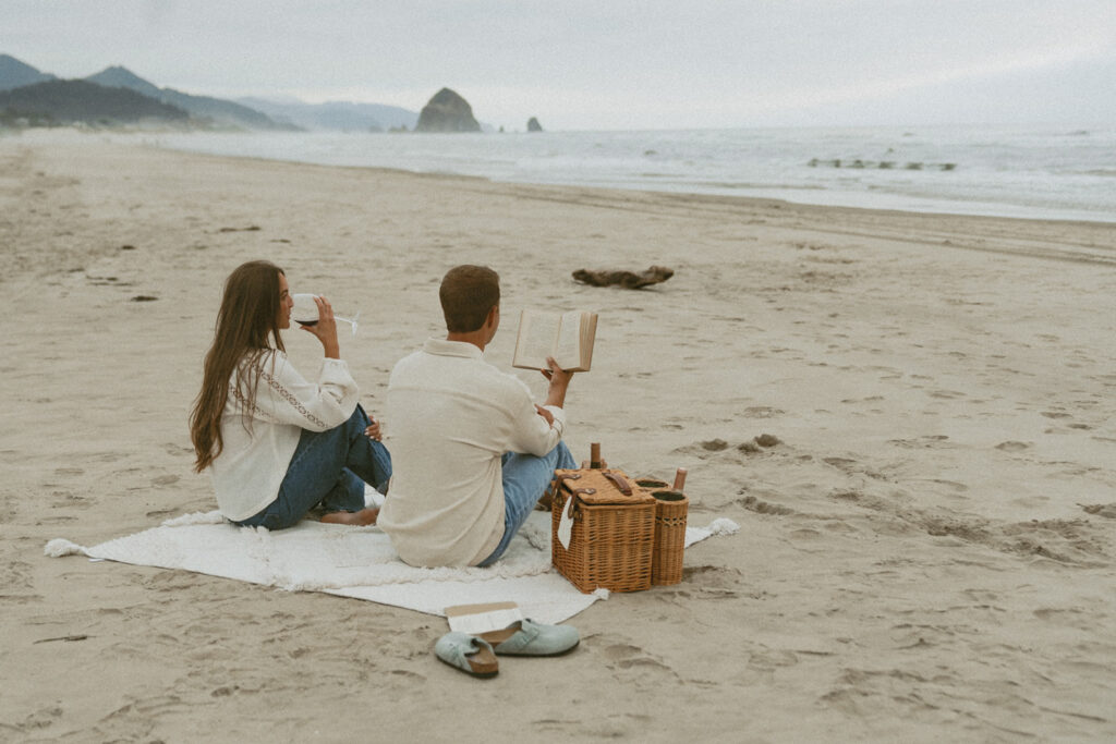 Couple sitting on a blanket at the beach reading and drinking wine