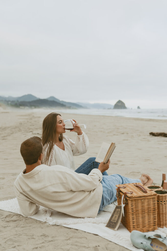 Couple sitting on a blanket at the beach with wine and a picnic basket