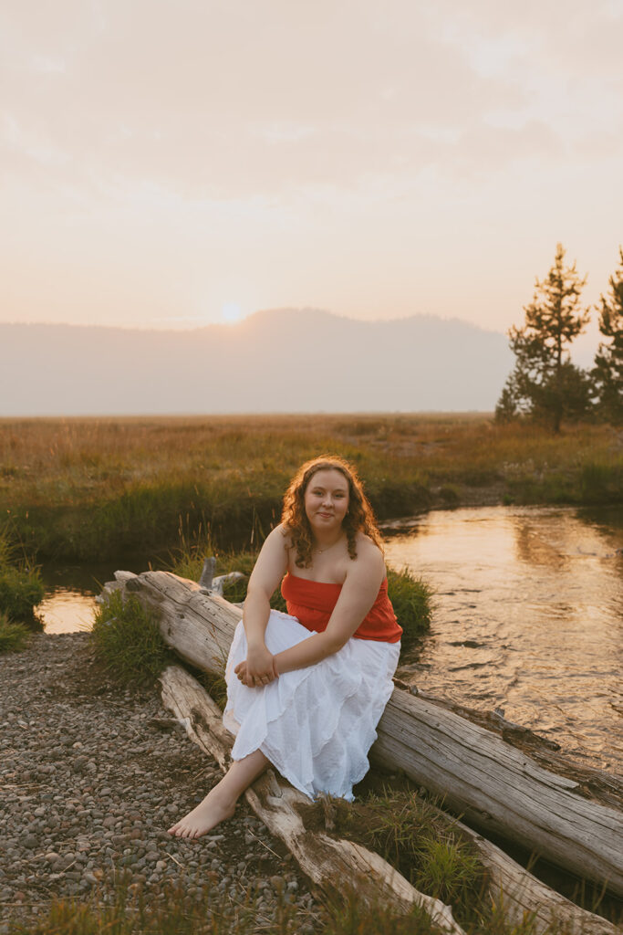 Woman wearing red top sitting on a log near the lake