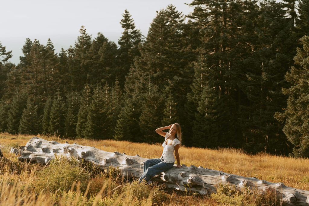 Senior photo of girl sitting on fallen tree with forest backdrop in Salem Oregon