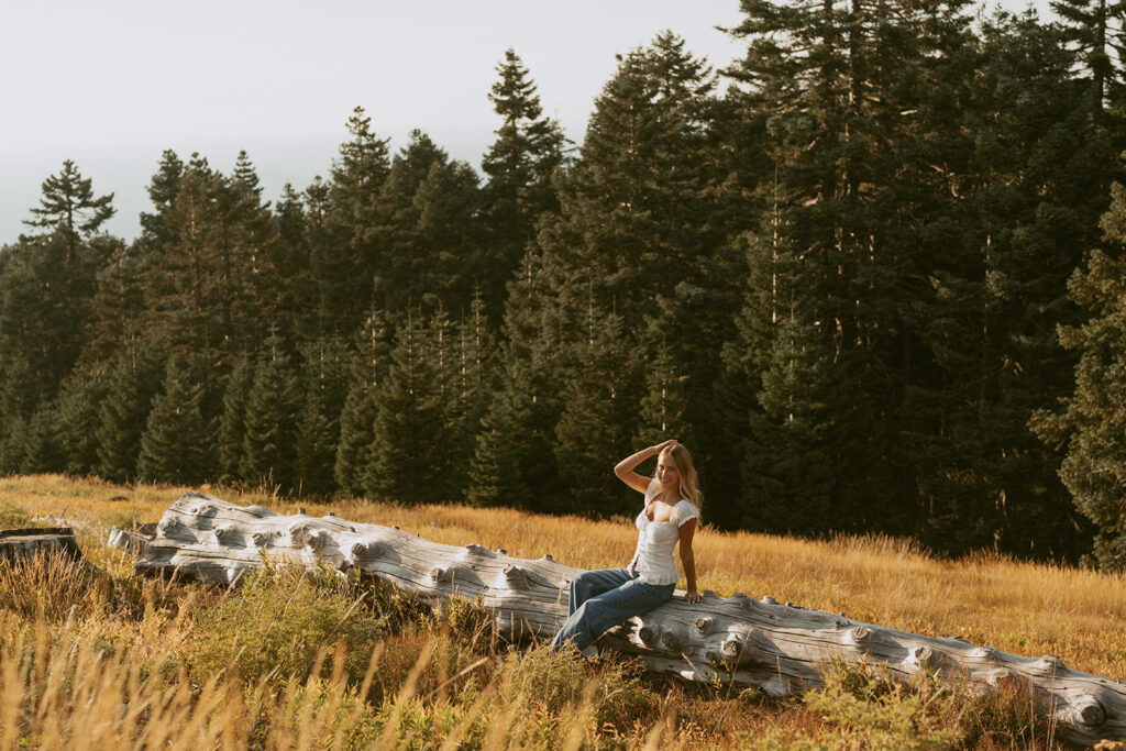 Senior girl sitting on log in open field at golden hour in Salem Oregon