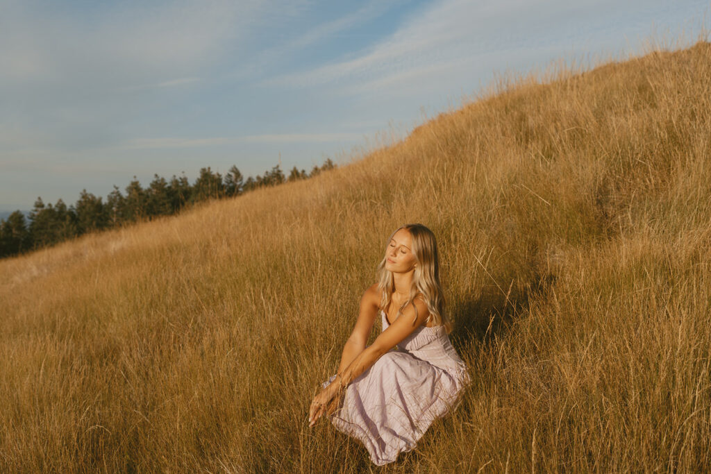 Senior girl in a lavender dress sitting in a golden field at sunset in Salem Oregon