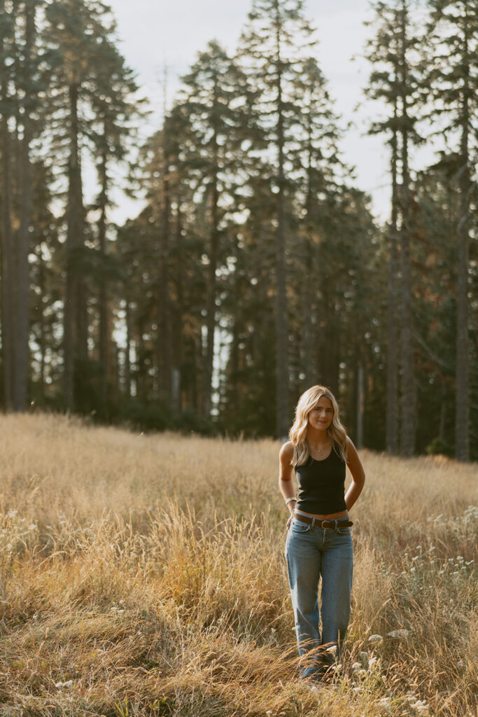 Senior photo of a girl standing in tall grass with forest background