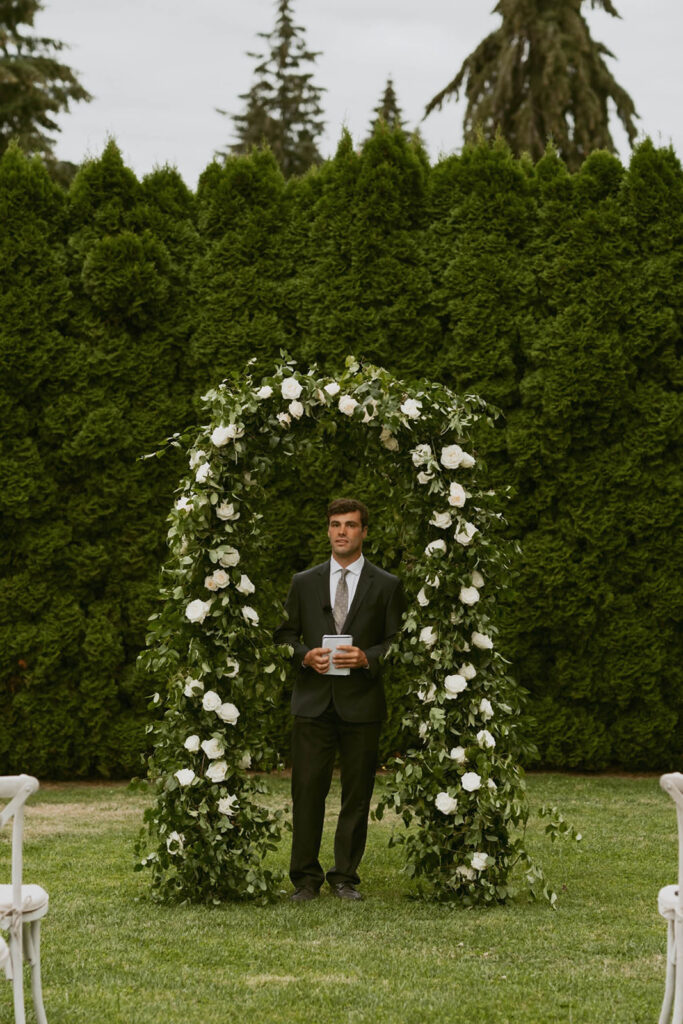 Officiant standing under floral arch at backyard venue