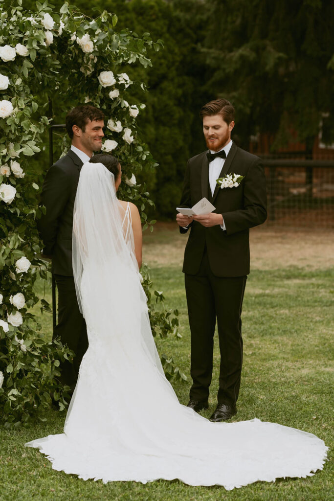 Groom reading vows to bride under floral arch