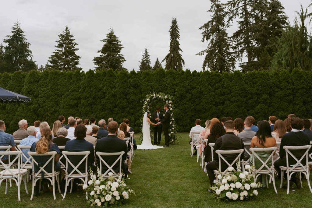 Bride and groom standing under floral arch during vows