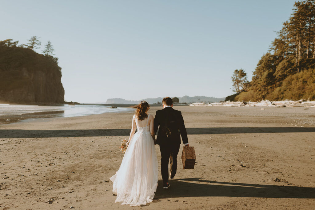 Bride and groom walking hand in hand on Oregon beach with picnic basket