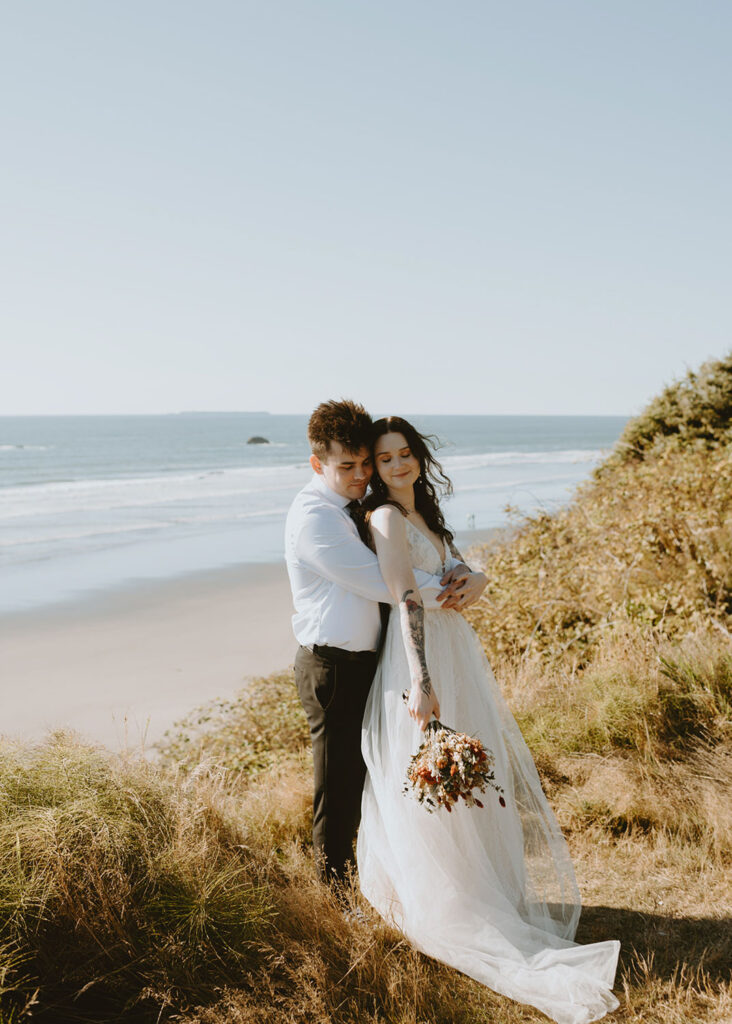 Bride and groom embracing on cliffside with ocean view in Oregon