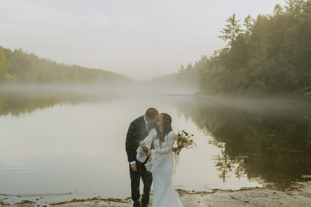 Couple kissing beside a misty Oregon lake during sunrise elopement