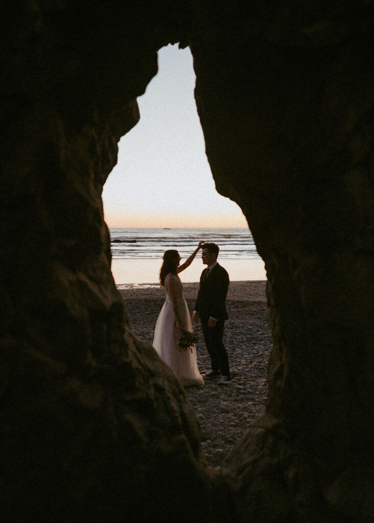 Bride and groom framed by rock arch during Oregon beach elopement